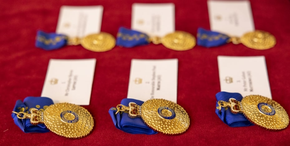 Rows of gold medals with blue ribbons sit on a red cloth. 