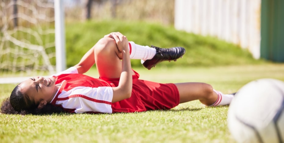 A female soccer player lay on the ground in pain and holding an injured knee. 