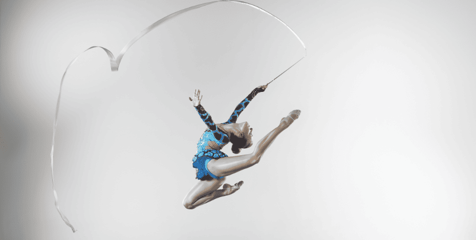 A rhythmic gymnast with a ribbon is leaping through the air. 