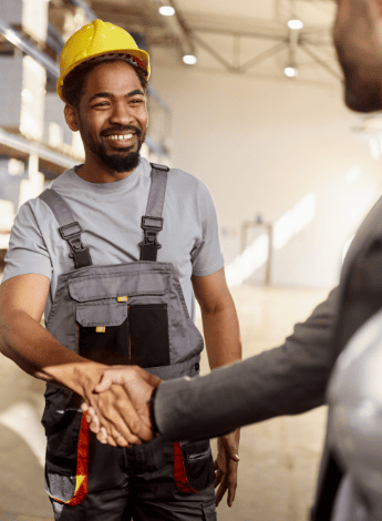A worker wearing a hardhat is shaking hands with a colleague. 