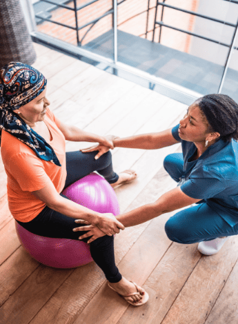 The image shows a physiotherapist helping a cancer patient use an exercise ball