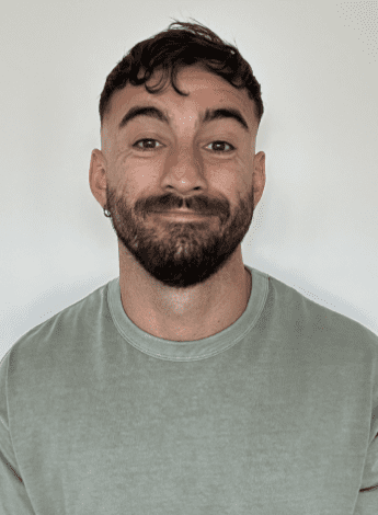 An Aboriginal man is wearing a light green t shirt and smiling at the camera. He has a short beard. 