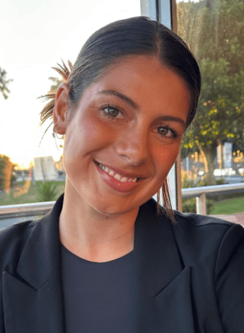 A woman with dark brown hair has tilted her head as she looks at the camera