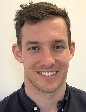 A man with short dark hair looks at the camera. He is wearing a black top.