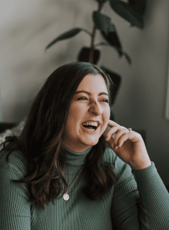 A woman with long hair is sitting in front of a plant and laughing