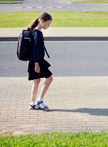 A young girl in school uniform and wearing a backpack is walking with a limp