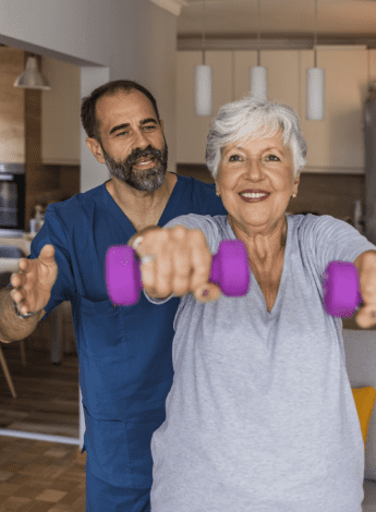 A carer is helping an older woman do an exercise using hand weights. 
