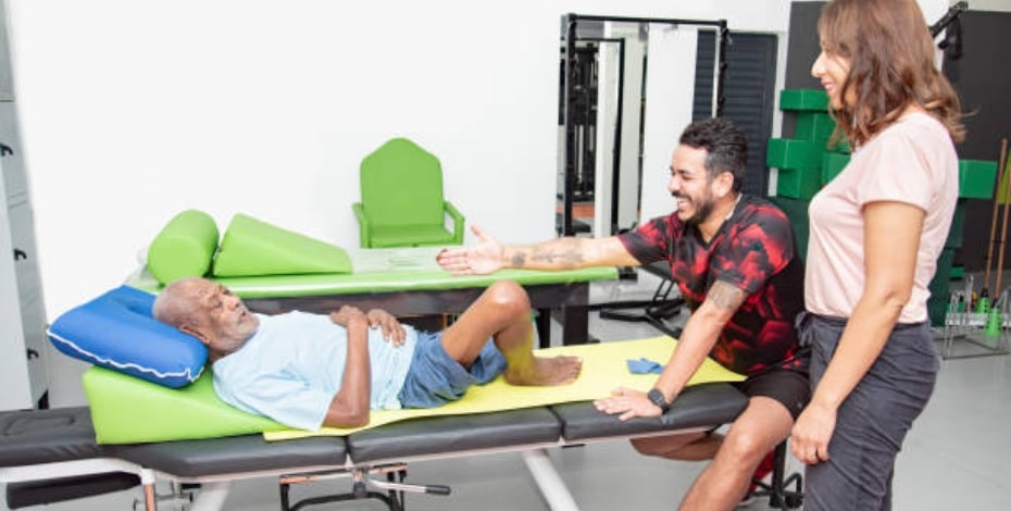 A woman looks on as a physio treats a man lying down. 