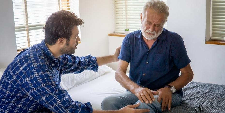 elderly man sitting on bed in aged care with younger male physio assessing his arm pain