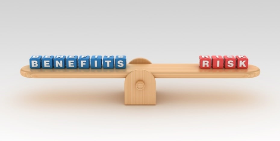Blue blocks spelling 'BENEFITS' and red blocks spelling 'RISK' balance on a wooden seesaw.