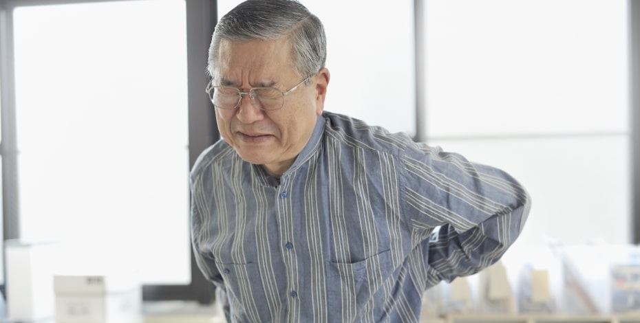 An elderly man clutches his lower back as if in pain. 
