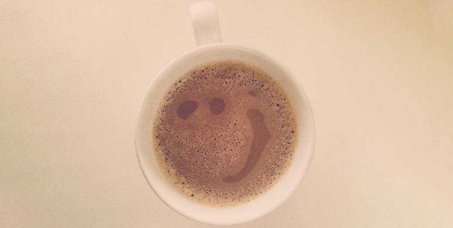 Aerial view of a white mug of coffee with a smiley face in the foam. 