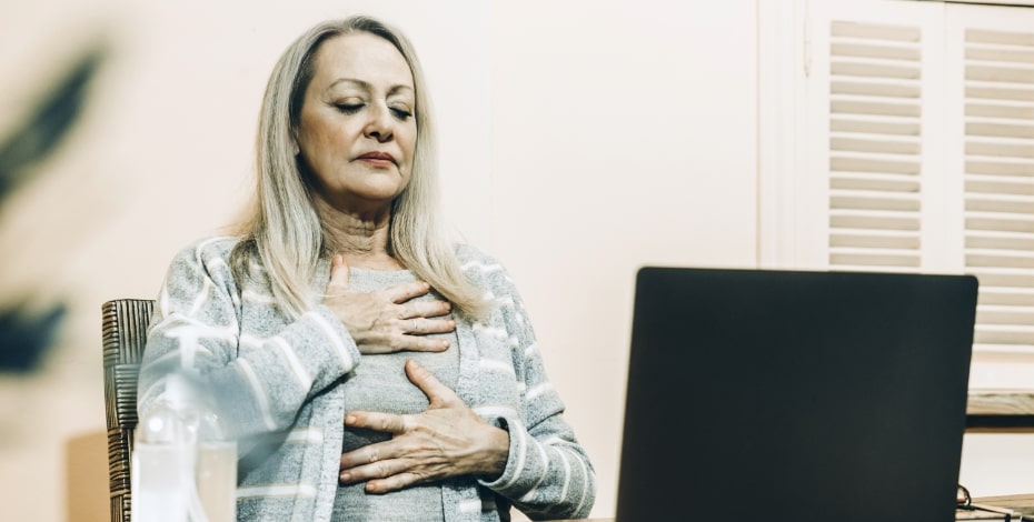 A woman sitting at a desk with her hands on her chest as if struggling to breathe.