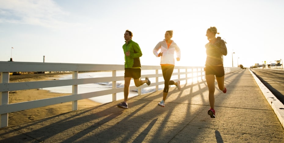Three people jogging on a pier at the beach.