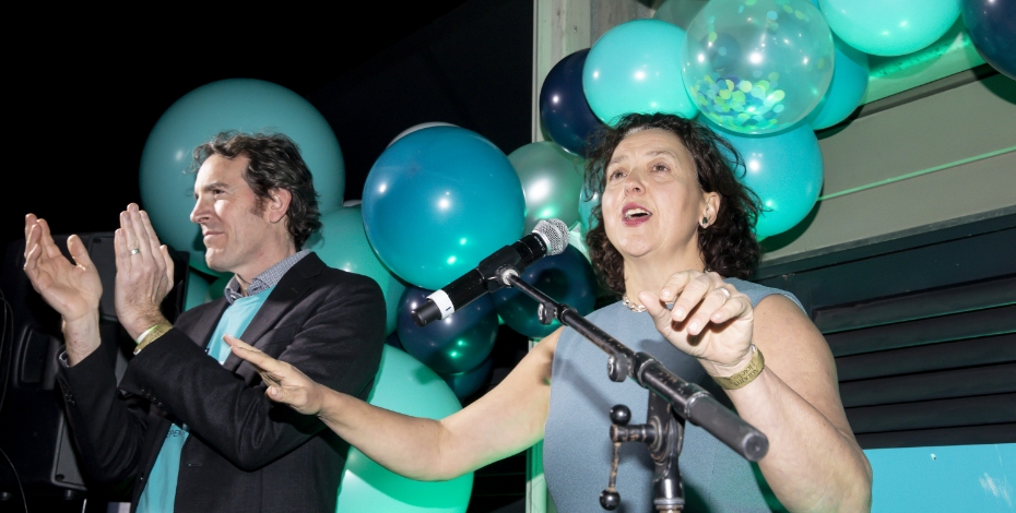 Monique Ryan on stage celebrating her election win, with teal balloons behind her. 