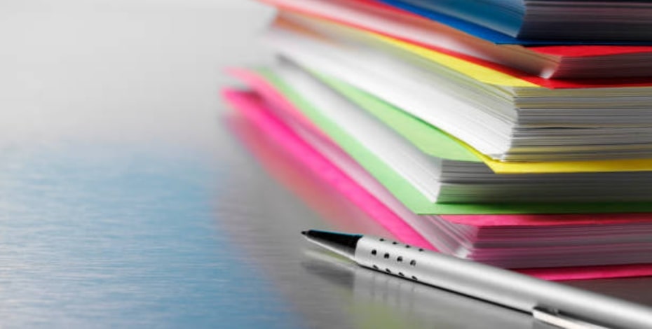 A silver pen lies next to a stack of different coloured folders. 