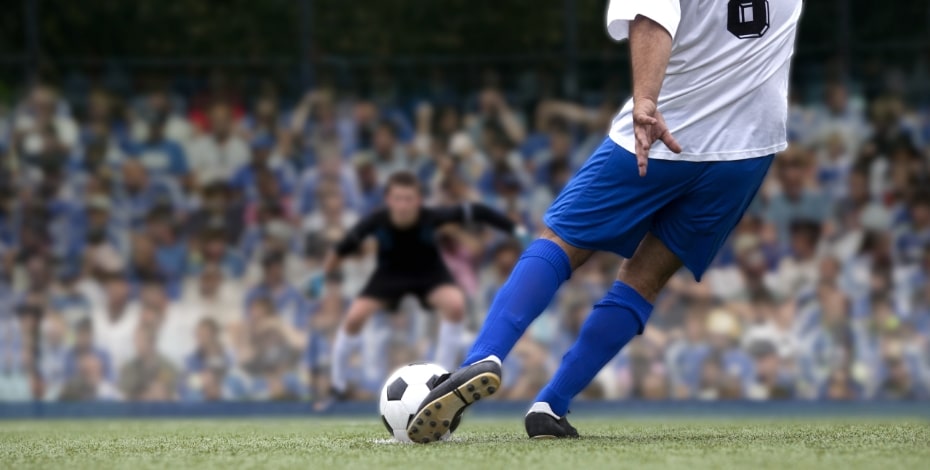 A soccer player in blue and white is about to take a free kick towards goal.