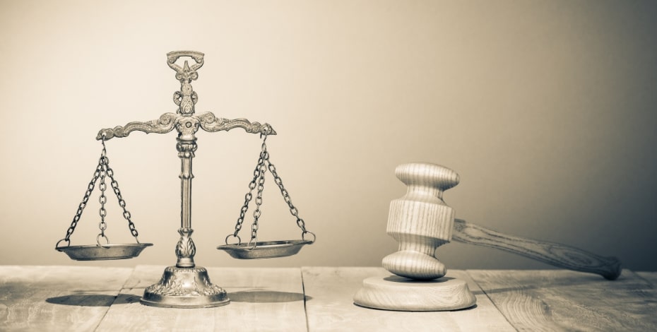 A silver set of old-fashioned scales sits beside a white wooden gavel on a wooden table.