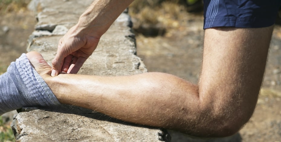 A leg stretched out backwards with a hand gripping the Achilles tendon area.