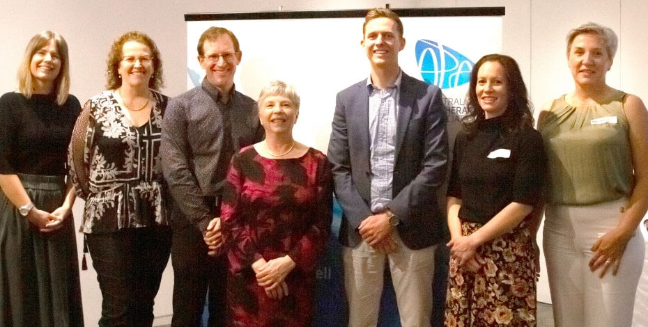 A group of men and women in business clothing stand in front of a board with the Australian Physiotherapy Association logo