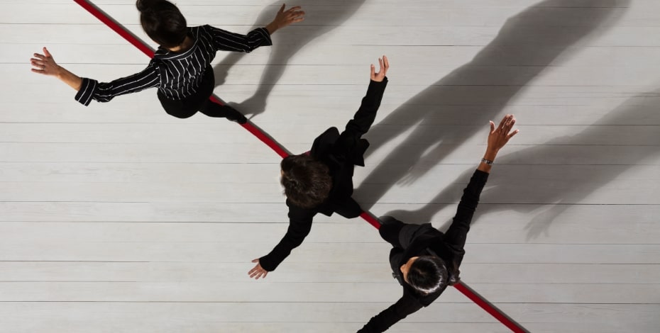 Three people dressed in black walk with arms stretched out to the sides along a red line on a white floor.