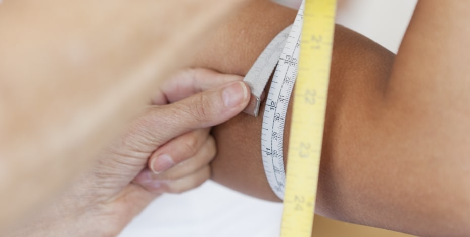 Close up of a tape measure being used to measure an upper arm.