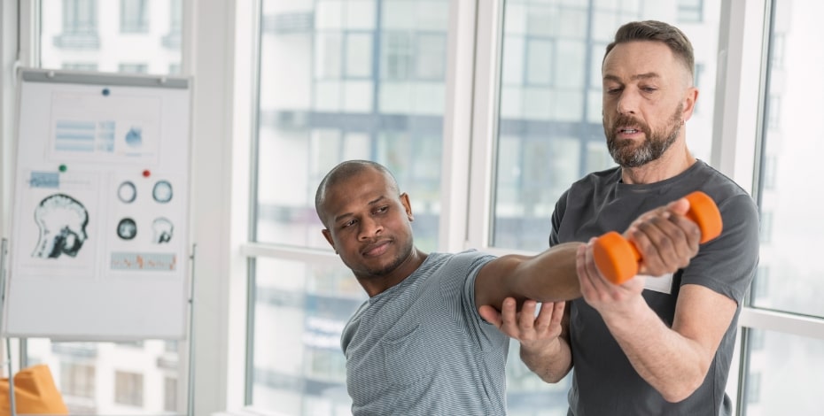 A physiotherapist assists a patient to perform an arm exercise holding a hand weight.