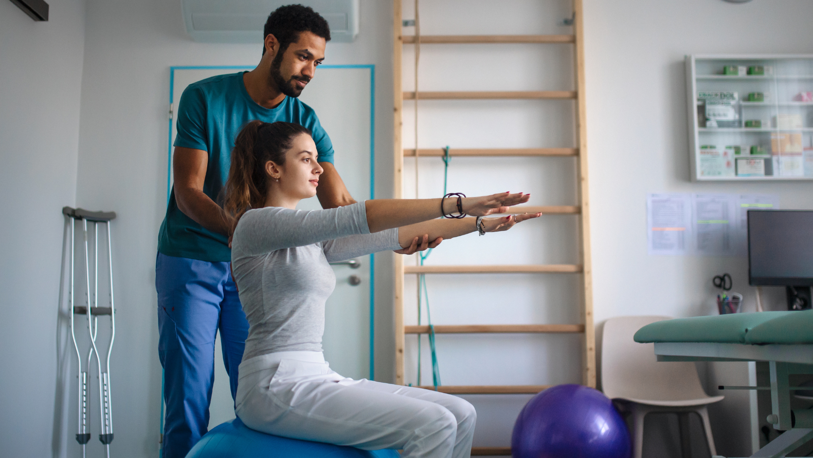 physiotherapist treats patient sitting on a fit ball there are crutches in the corner of the room