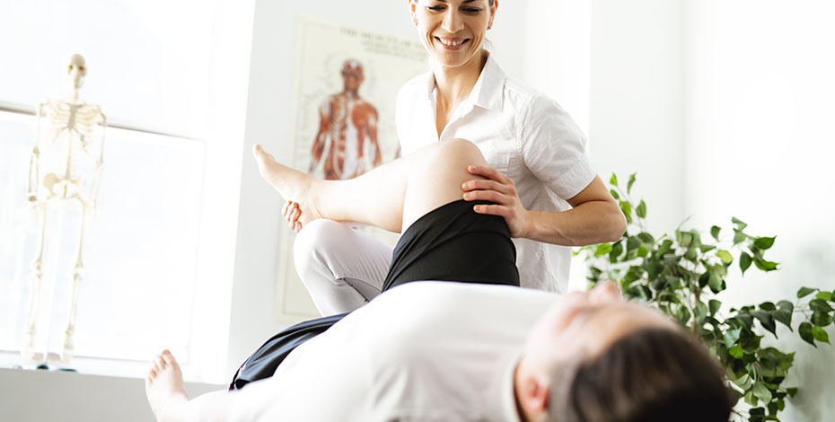 A physio works with a patient lying on their back and bending their knee.