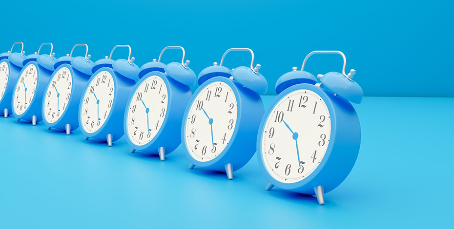 A row of bright blue old-fashioned alarm clocks against a blue floor and wall.