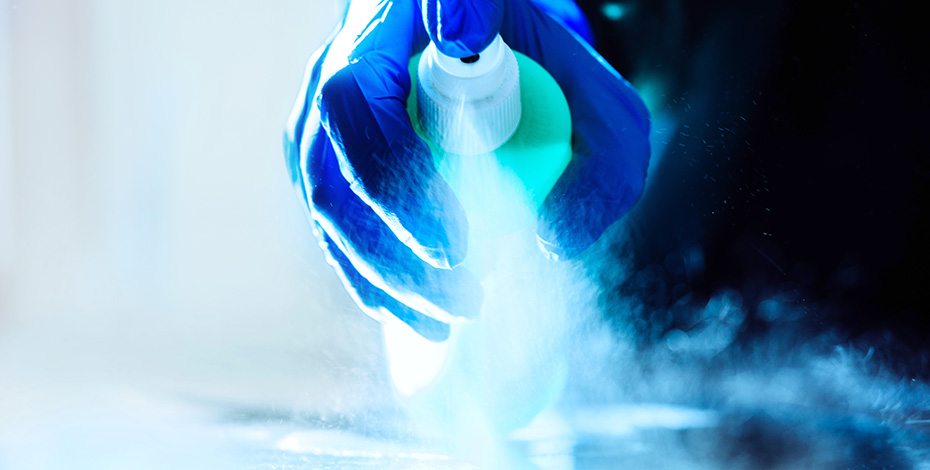 A gloved hand using a spray bottle showering some sort of liquid on to a bench top.