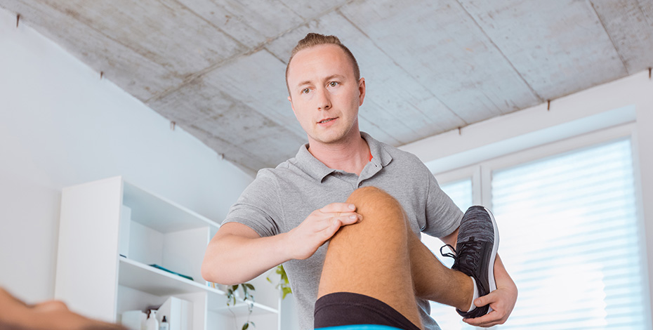 A physiotherapist bends a client's knee up towards his chest.