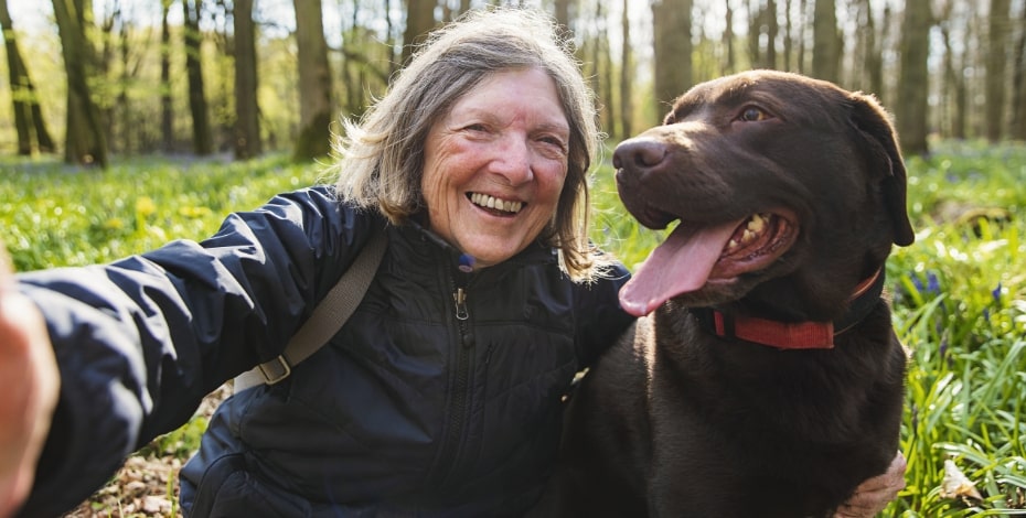 Active older woman smiles with her dog sitting in a forest.