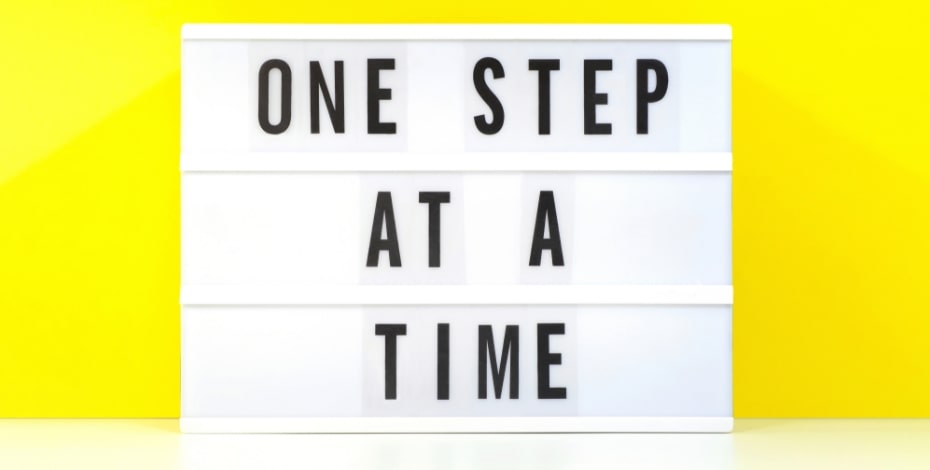 A white light box is on a yellow background. The words on it say 'One step at a time'. 