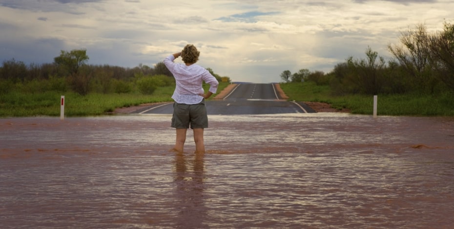 A woman in shorts is standing on a muddy flooded road and looking into the distance. 
