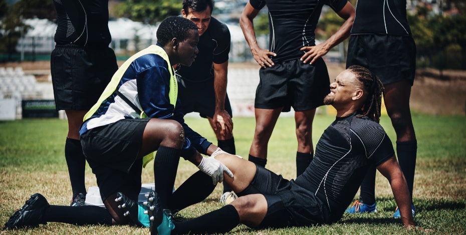 An injured rugby player is assessed on field with teammates nearby.