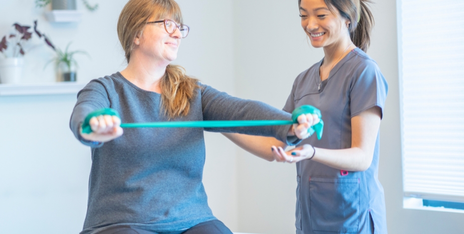 A physio smiling while a person uses a resistance band for therapy 