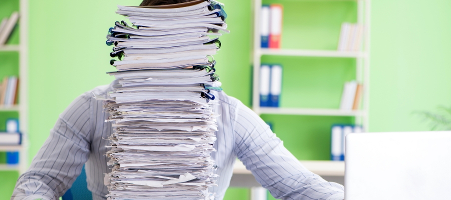 tall stack of papers on a desk covering the person so you can only see their arms