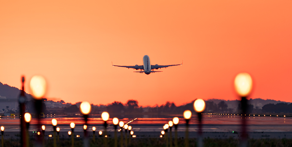 Image of a plane taking off from a runway against a beautiful sunset sky.