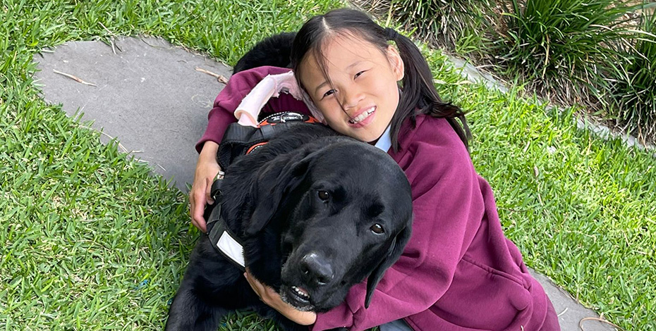 Young patient Chloe cuddles Checkers, a gait training dog. Checkers is black and gorgeous. 
