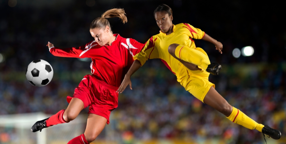 two women jumping in air to make contact with a soccer ball
