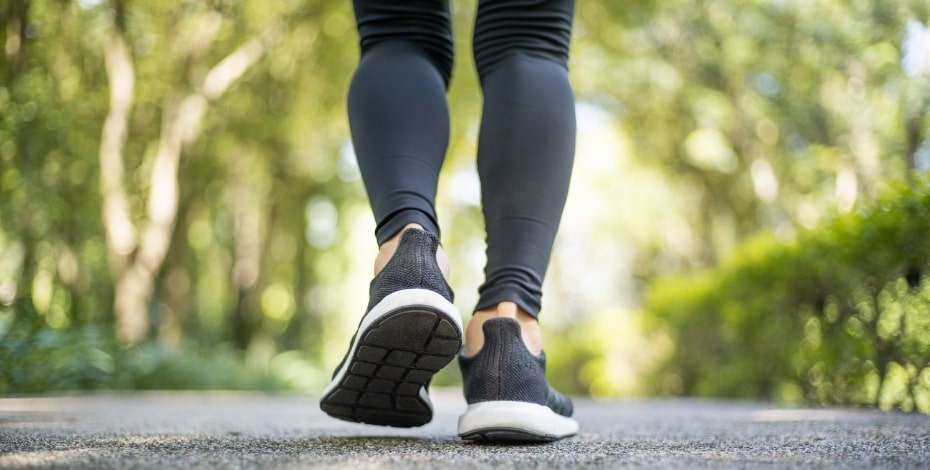 The image shows the lower legs of someone walking away from the camera. They are wearing grey leggings and grey walking shoes. 