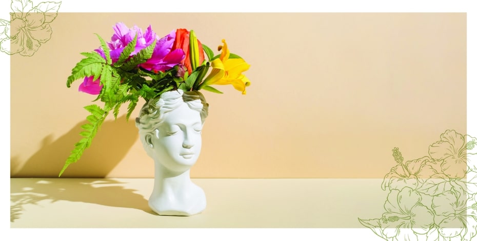 A statuesque head shaped vase with flowers in it. in front of a brown wall 