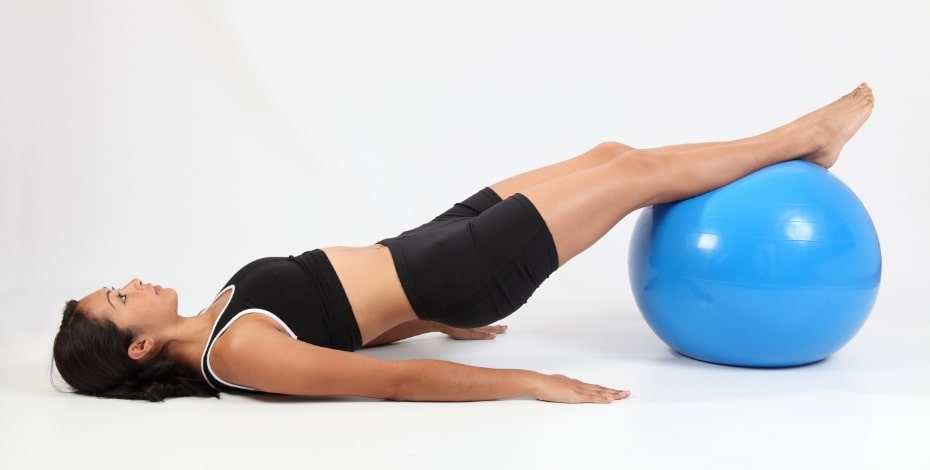 A woman is stretched out on a blue exercise ball.