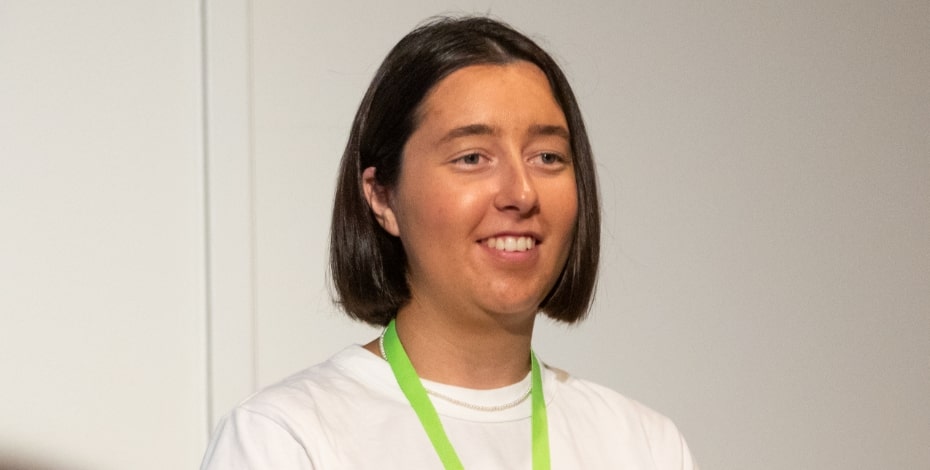 A woman with dark hair in a bob, wearing a white shirt. She has a green lanyard around her neck. 