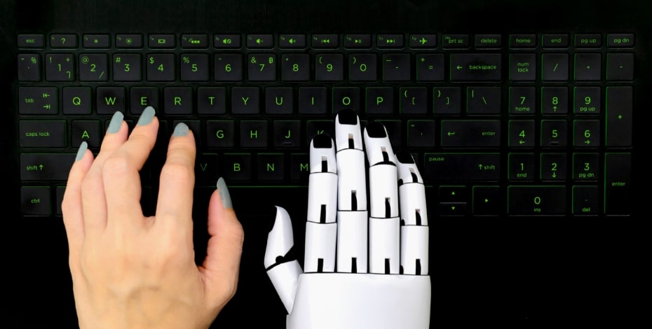A human hand rests next to a robot hand on a computer keyboard.