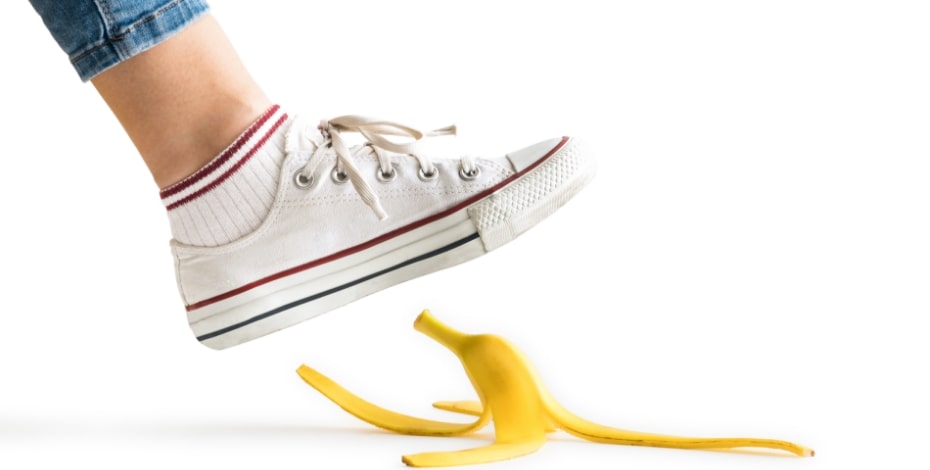 foot and ankle in white sneaker stepping on yellow banana skin