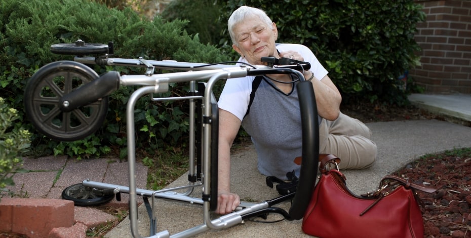 Older person half lying on the ground, holding a walker
