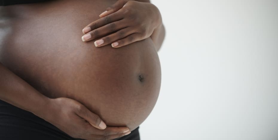 The picture shows a pregnant woman's belly. She is cradling it with her hands.