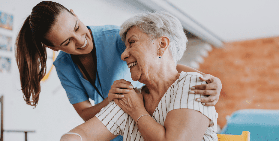 A healthcare professional and an elderly woman smile at each other. 